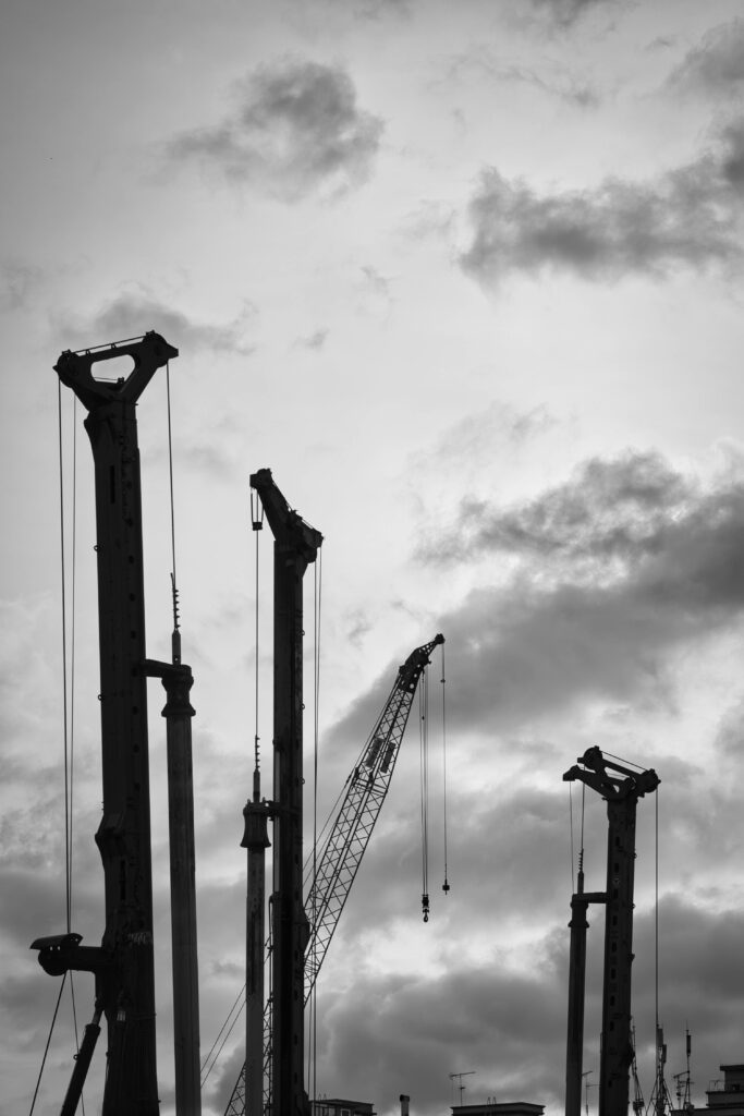 pexels-photo-12879119-12879119 Black and white image of cranes silhouetted against a dramatic cloudy sky, capturing industrial construction.